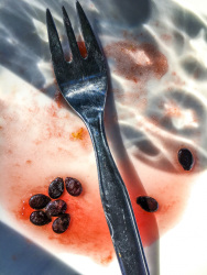a silver fork is laying on a white plate with red juice and seeds of a watermelon