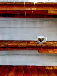 a coffeecup with a golden heart is staying in a light brown shelf