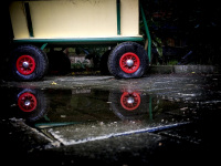 a yellow handcart with red wheels ist reflecting in a puddle