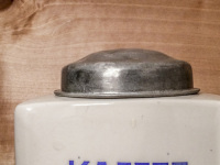 an old ceramic coffee grinder with a silver lid and blue lettered kaffee