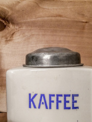 an old ceramic coffee grinder with a silver lid and blue lettered kaffee