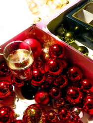 a full glass of sparkling wine is standing between red, green and golden christmas balls