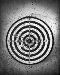 a very perforaded dart board with some darts, black-and-white