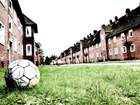 an old football is laying in grass at the street between red brick houses in unterlüß
