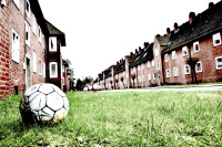an old football is laying in grass at the street between red brick houses in unterlüß