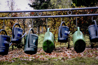 green and blue watering cans are hanging on a black steel railing at a cemetry in bergen in lower saxony