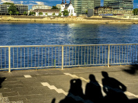 the shadows of three people at the shore promenade at the rhine in cologne