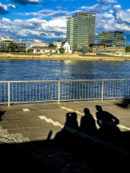 the shadows of three people at the shore promenade at the rhine in cologne