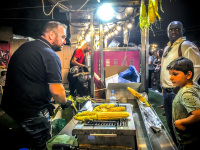 a man at a stand at the funfair in kremasti on rhodes grills corncobs for customers