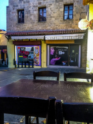 in front you see an empty wooden table with chairs and in the background two store windows in an empty street in the old town of rhodes in the evening