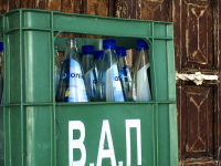 in front of a brown wooden door in lindos on rhodes is standing an old green vap drinks crate with blue bottles