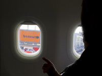 the index finger of a passagier in a plane point to the window where you see lettering tomatensaft on a sign at the catering