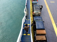 left the sea, right cars on the ferry and in the middle a woman goes downstairs the steps on the ferryboat rio antirrio