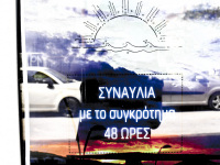 in a glass door of a store in aegion is hanging a plakat for a sunsetfestival, two cars are reflecting in the glassdoor