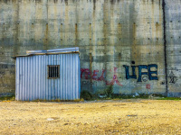 in diakopto stands a blue construction hut on yellow grass and in front of a grey wall with graffiti
