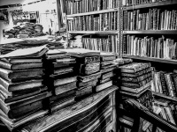 a collection of old books are standing and laying in a shop of antiquarian in monastiraki in athens, black-and-white