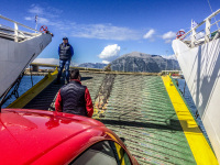 you see two men, a blue sky, a red car roof and the green loading flap of a ferry at patras