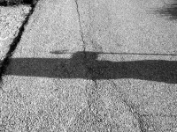 on a street in diakopto there is the shadow of a person who is holding a shepherd\'s stick, black-and-white