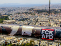 in front of a big view over athens with the acropolis there is a sticker at a railing on the lycabettus hill with lettering fckafd