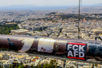 in front of a big view over athens with the acropolis there is a sticker at a railing on the lycabettus hill with lettering fckafd