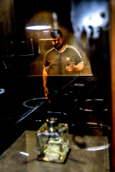 behind the reflexion of some stuff in a restaurant on the lycabettus hill stands a young greek with his phone