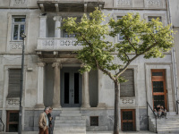 the front of a house in classicism style in makrygianni in athenswith a green tree and some passing people