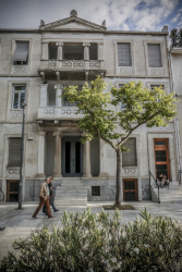 the front of a house in classicism style in makrygianni in athenswith a green tree and some passing people