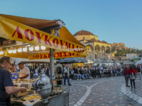 a stand with fresh baking loukoumades and many people on the monastiraki square in athens