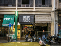 a taxi is passing a street with stores and motorcycles in monastiraki in athens
