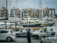 a man is walking alone against the traffic on the street next to the harbor pasalimani in piraeus