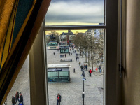 through a window in the hotel XII apostel you see the heumarkt in cologne in germany where some people are going for a walk
