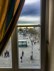 through a window in the hotel XII apostel you see the heumarkt in cologne in germany where some people are going for a walk