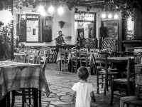 in the tavern pelikanos in vati on rhodes a little child is standing between the chairs and looks at the music band, black-and-white