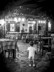 in the tavern pelikanos in vati on rhodes a little child is standing between the chairs and looks at the music band, black-and-white