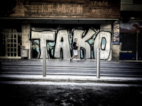 on a street in athens a man is passing a big graffiti at a wall