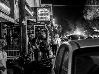 an illuminated street in kremasti on rhodes with many signs of restaurants and pedestrians by night, black-and-white