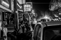 an illuminated street in kremasti on rhodes with many signs of restaurants and pedestrians by night, black-and-white