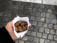 a man who ist standing on cobblestones near the acropolis in athens holds a little paper bag with nuts