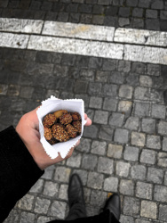 a man who ist standing on cobblestones near the acropolis in athens holds a little paper bag with nuts