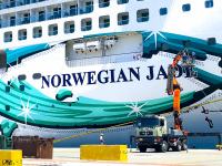 a truck with crane seems very small in front of a cruise ship norwegian jade in the harbor of rhodes