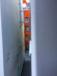 through two white housewalls you see a little part of an orange house in the salzgasse in cologne
