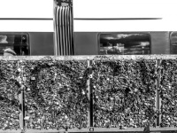 behind a wall full of padlocks at the hohenzollernbrücke in cologne drive past a train, black-and-white