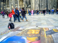 a painted picture of jesus on the floor in front of the dom in cologne where tourists are walking around