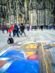 a painted picture of jesus on the floor in front of the dom in cologne where tourists are walking around