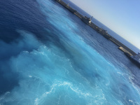 in front is foam in the turquoise sea, in the background are grey military ships at the harbor of rhodes
