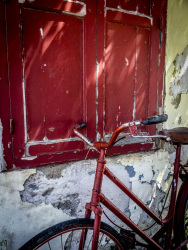 an old red bike is standig in forward to a red wooden window in the old town of rhodes
