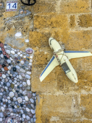 at a yello wall in the old town of rhodes is hanging the housenumber 14, a little plane and a mosaic of stones