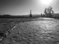 in front is the wall of the tsambika church of rhodes, in the background a holy bell and a sunset, black-and-white