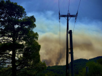 an electricity pole is standing in front of the big fire in apollona on rhodes in 2023, a big yellow clowd of smoke is in the background