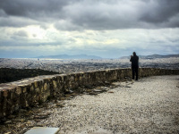 a man in black is standing on the platform of the acroplis in athens to take a picture of the metropolis